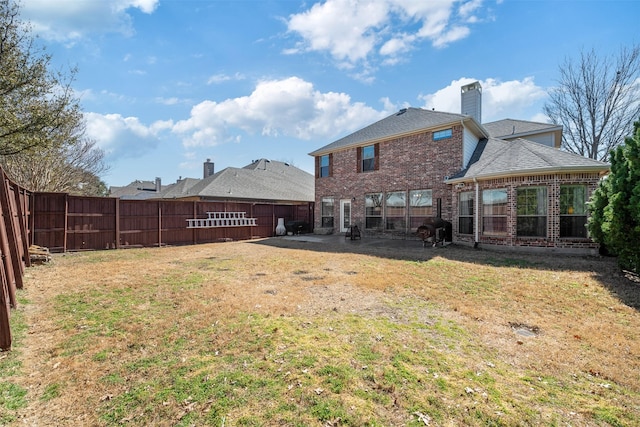 back of property featuring a patio, a fenced backyard, brick siding, a yard, and a chimney