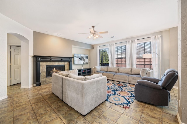 living area with arched walkways, visible vents, ceiling fan, a tile fireplace, and baseboards