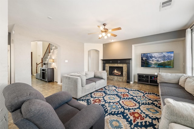 living room with arched walkways, ceiling fan, a fireplace, visible vents, and stairway