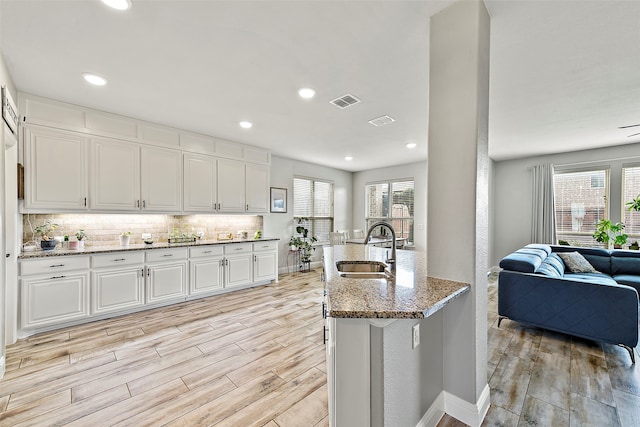 kitchen with light wood-style flooring, light stone countertops, a sink, a wealth of natural light, and decorative backsplash