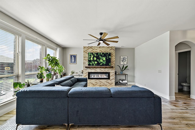 living area with baseboards, arched walkways, ceiling fan, wood finished floors, and a fireplace