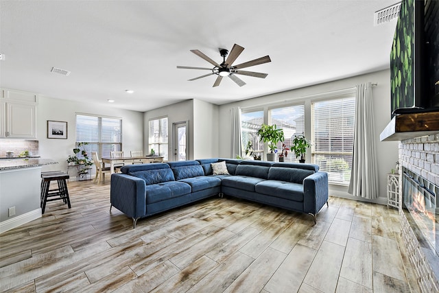 living room with a wealth of natural light, a glass covered fireplace, visible vents, and light wood-style floors