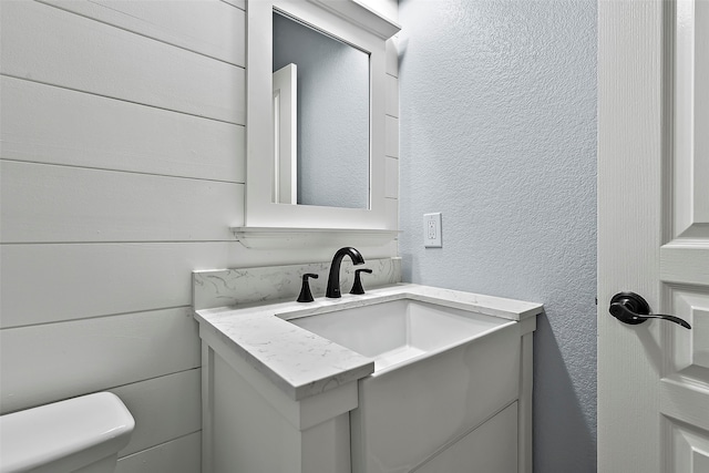 half bath featuring a textured wall, vanity, and toilet