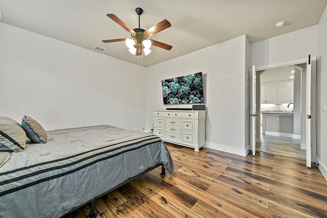 bedroom with ceiling fan, wood finished floors, visible vents, and baseboards