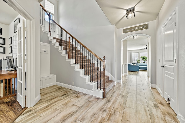 entryway with arched walkways, ceiling fan, baseboards, stairway, and light wood-type flooring