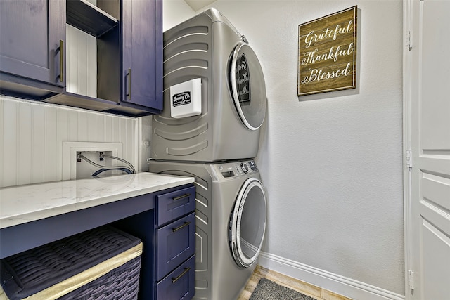 washroom featuring a textured wall, stacked washing maching and dryer, cabinet space, and baseboards