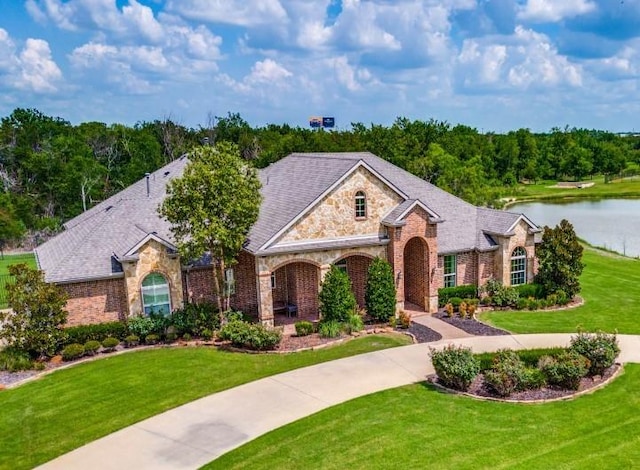 view of front of home with a water view, brick siding, driveway, and a front yard