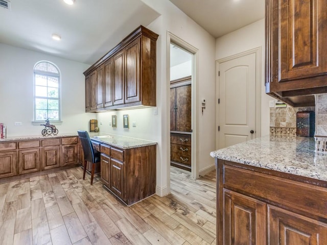 kitchen featuring light wood-style floors, built in desk, decorative backsplash, and light stone countertops