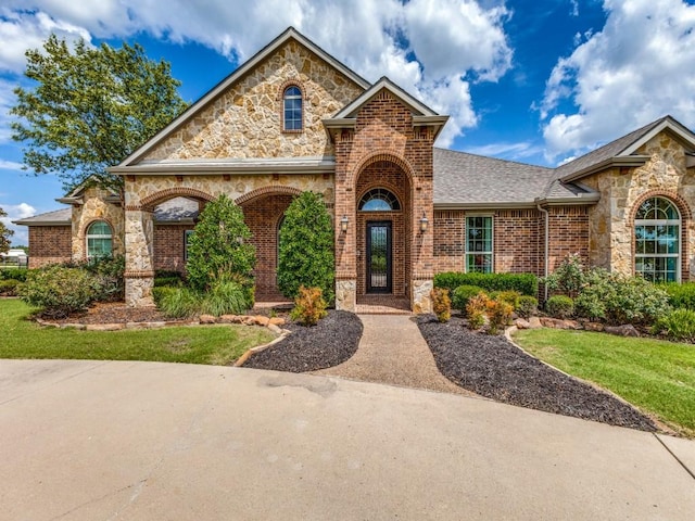 view of front of home with a shingled roof, stone siding, brick siding, and a front lawn