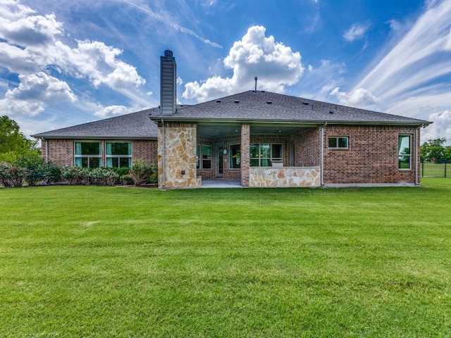 rear view of house featuring stone siding, a patio area, a yard, and a chimney