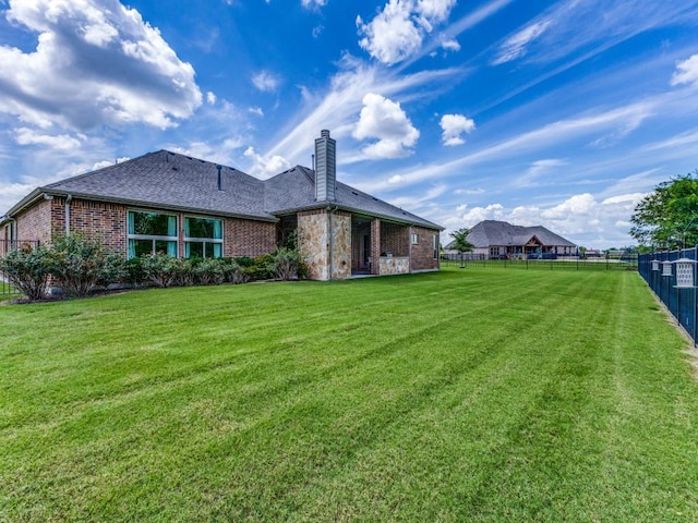 back of property with a yard, brick siding, a chimney, and fence