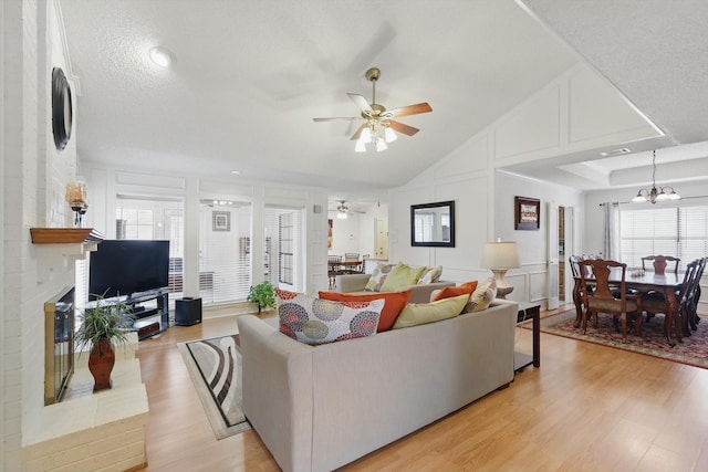 living area featuring light wood finished floors, a decorative wall, a textured ceiling, and ceiling fan with notable chandelier