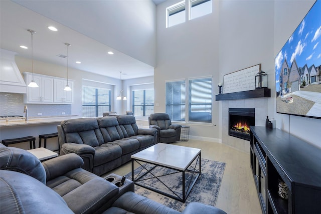 living room featuring recessed lighting, a high ceiling, baseboards, light wood-type flooring, and a tiled fireplace