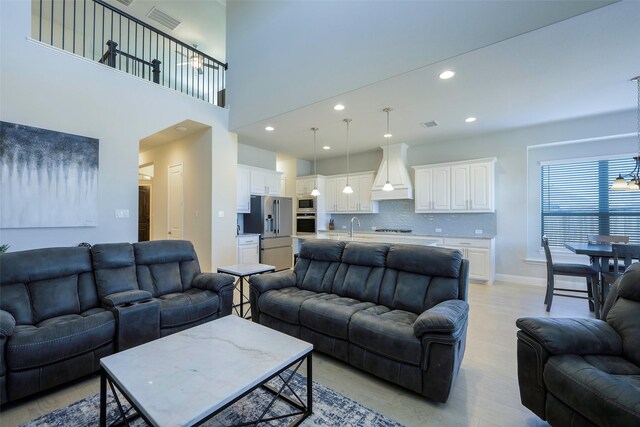living area with light wood-style flooring, recessed lighting, a high ceiling, visible vents, and baseboards