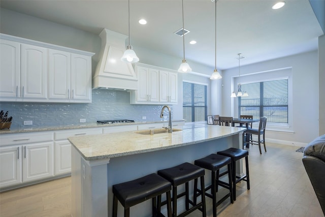 kitchen with a sink, backsplash, custom exhaust hood, and visible vents