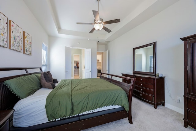 bedroom with a raised ceiling, light colored carpet, ensuite bathroom, ceiling fan, and baseboards