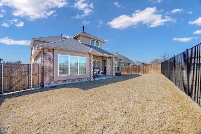 back of house featuring brick siding, a lawn, a fenced backyard, and roof with shingles
