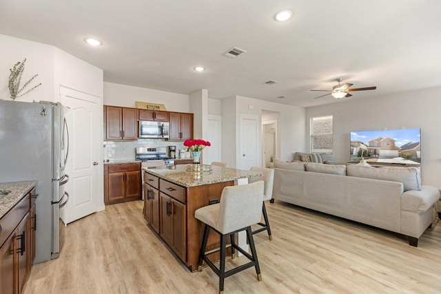 kitchen with a breakfast bar, stainless steel appliances, visible vents, light wood-style flooring, and a kitchen island