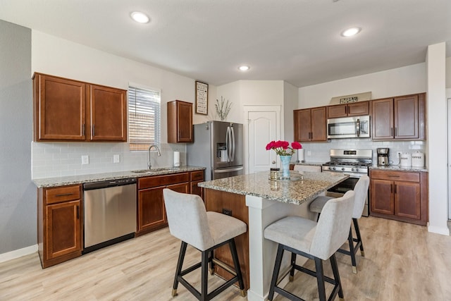 kitchen featuring a breakfast bar, light stone countertops, stainless steel appliances, light wood-style floors, and a sink