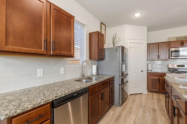 kitchen featuring light stone counters, stainless steel appliances, a sink, light wood-style floors, and tasteful backsplash