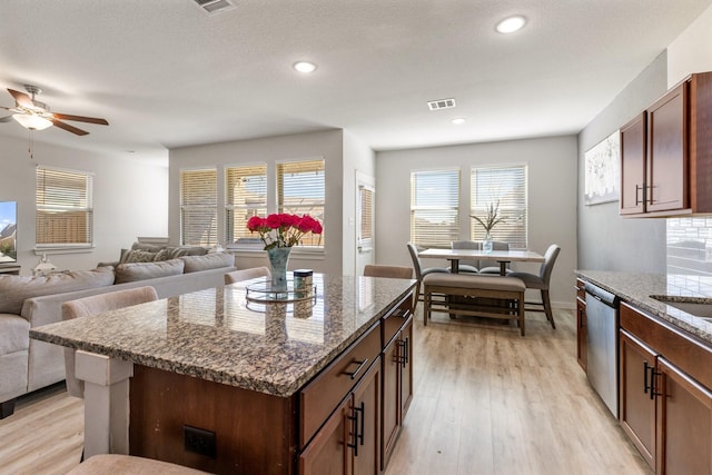 kitchen with visible vents, stainless steel dishwasher, open floor plan, light wood-type flooring, and dark stone counters