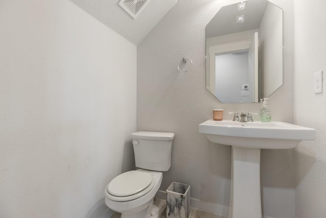 half bath featuring toilet, baseboards, and visible vents