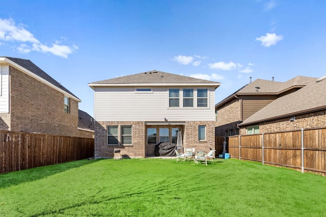 back of property with a fenced backyard, a lawn, and brick siding