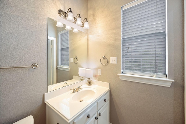 half bath featuring toilet, a textured wall, and vanity