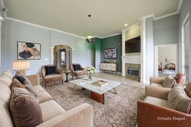 living area with arched walkways, crown molding, decorative columns, a tiled fireplace, and tile patterned floors