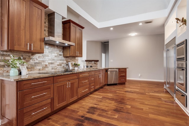 kitchen featuring built in appliances, a sink, visible vents, wall chimney exhaust hood, and tasteful backsplash