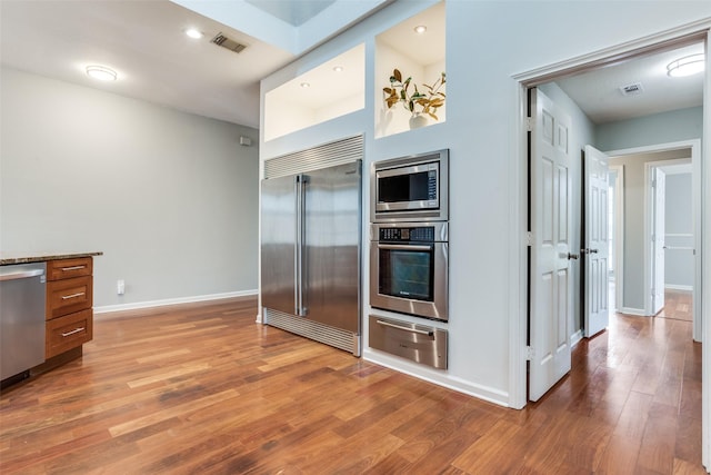 kitchen featuring baseboards, visible vents, wood finished floors, built in appliances, and a warming drawer