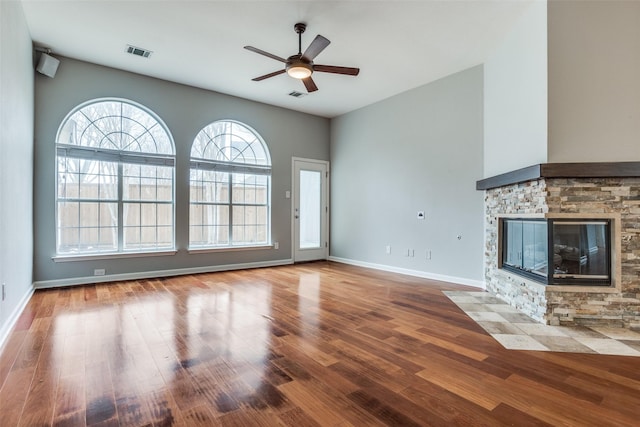 unfurnished living room featuring a fireplace, wood finished floors, visible vents, and a ceiling fan