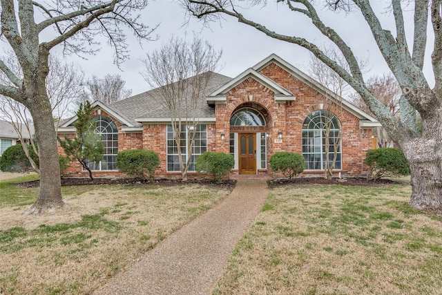 view of front of house with brick siding, roof with shingles, and a front yard