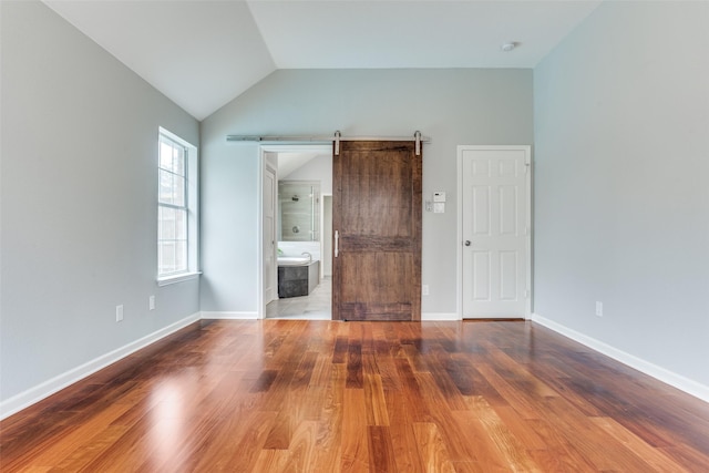 interior space with vaulted ceiling, a barn door, wood finished floors, and baseboards