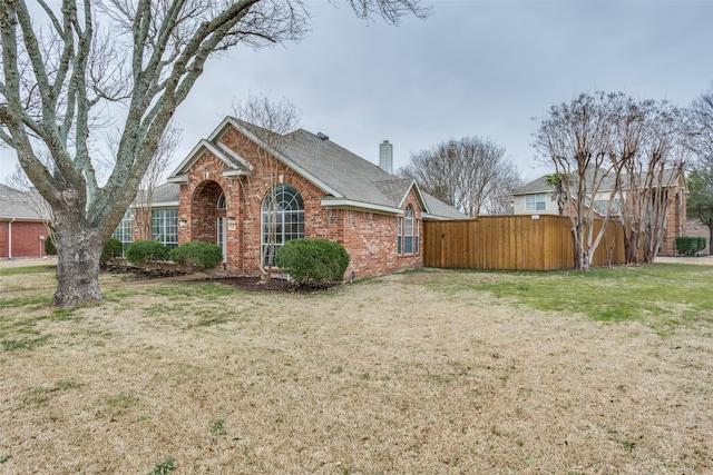 view of property exterior featuring brick siding, a lawn, a chimney, and fence