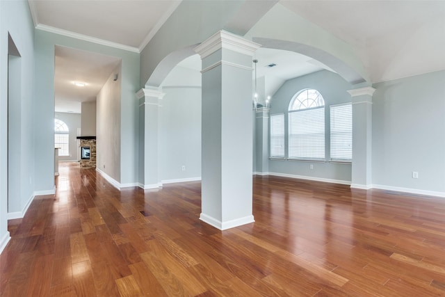 unfurnished living room with plenty of natural light, decorative columns, a stone fireplace, and wood finished floors