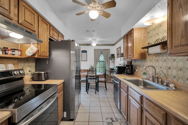 kitchen featuring stainless steel appliances, light countertops, light tile patterned flooring, a sink, and under cabinet range hood