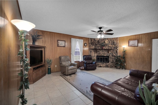 living area featuring a fireplace, light tile patterned floors, ceiling fan, wooden walls, and a textured ceiling