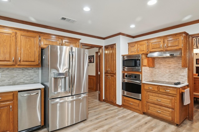 kitchen with under cabinet range hood, light countertops, appliances with stainless steel finishes, wainscoting, and brown cabinetry