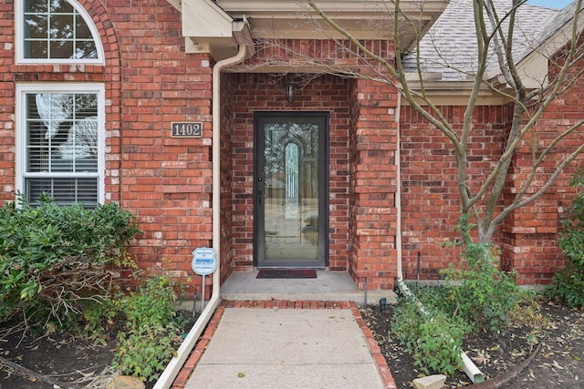 entrance to property featuring brick siding and roof with shingles