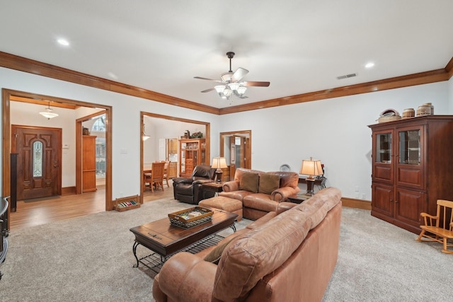 living area with light colored carpet, visible vents, ornamental molding, a ceiling fan, and baseboards