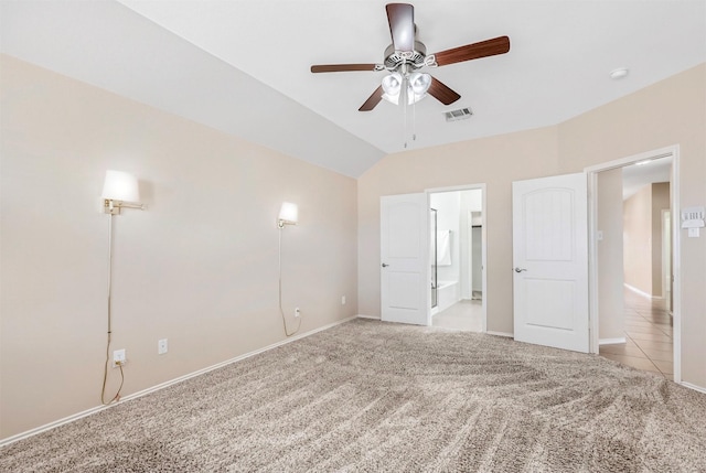 unfurnished bedroom featuring visible vents, light colored carpet, vaulted ceiling, ensuite bath, and a ceiling fan