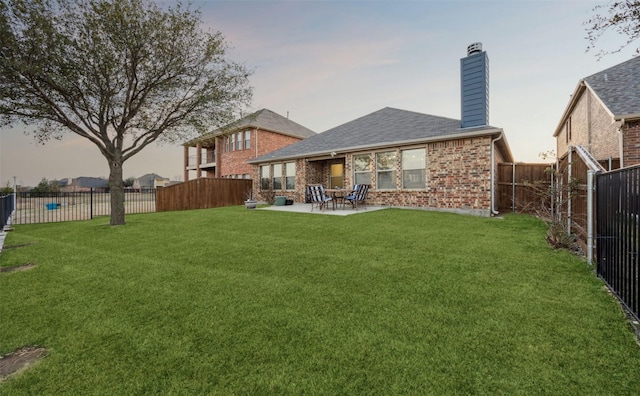 rear view of property featuring a yard, a fenced backyard, a chimney, a patio area, and brick siding