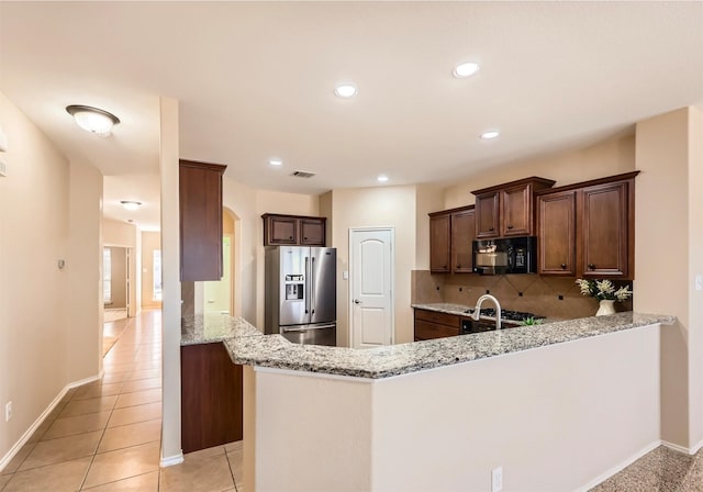 kitchen featuring tasteful backsplash, visible vents, black microwave, light stone counters, and stainless steel fridge