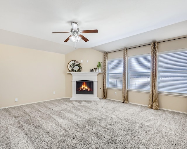 unfurnished living room with a ceiling fan, baseboards, a fireplace with flush hearth, vaulted ceiling, and carpet flooring