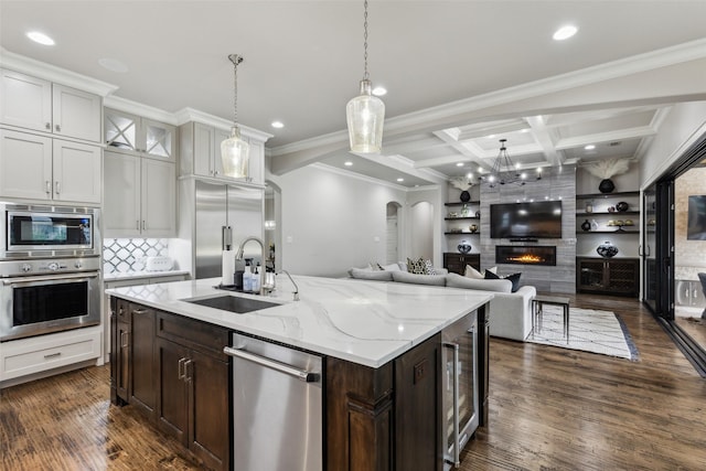 kitchen featuring built in appliances, arched walkways, coffered ceiling, a fireplace, and a sink