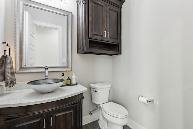 half bathroom with baseboards, vanity, and toilet