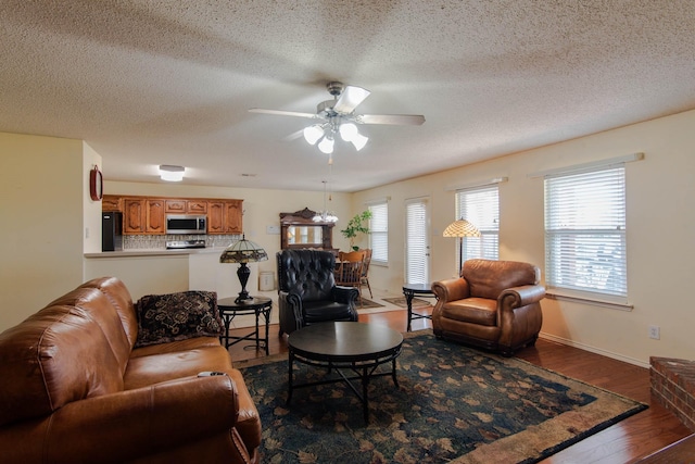 living area featuring baseboards, a textured ceiling, a ceiling fan, and wood finished floors