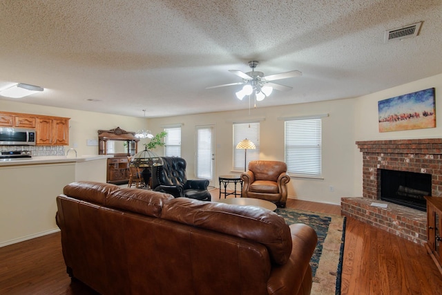 living area with a fireplace, visible vents, ceiling fan, a textured ceiling, and wood finished floors