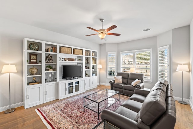 living area with visible vents, ceiling fan, baseboards, and wood finished floors